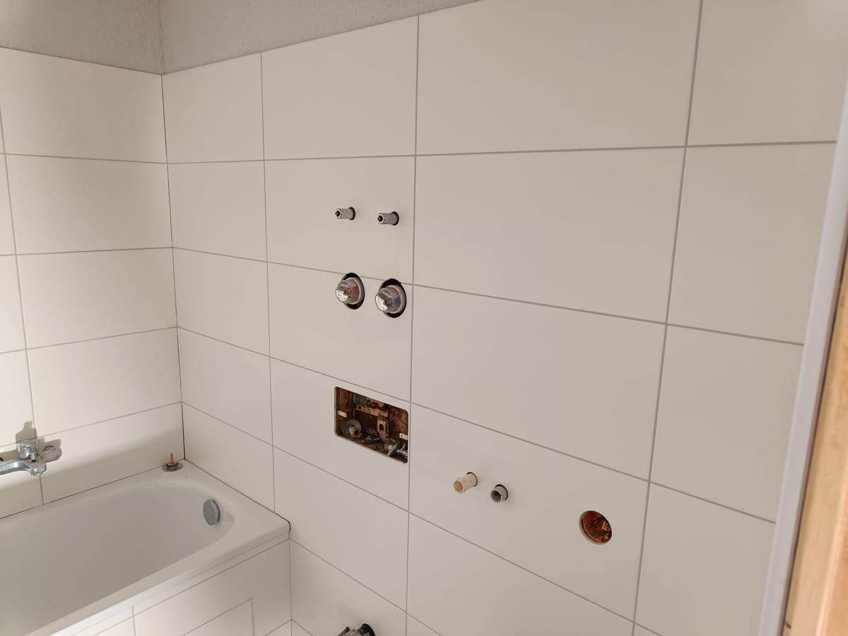 Wandanschlüsse für Armaturen über einer Badewanne in einem weiß gefliesten Bad